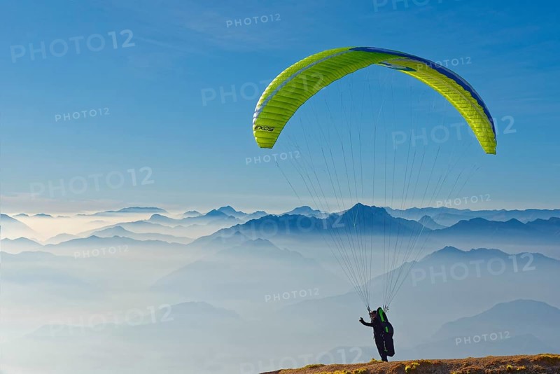 Paraglider taking off with the peaks of the Lake Garda mountains and Bergamo Alps