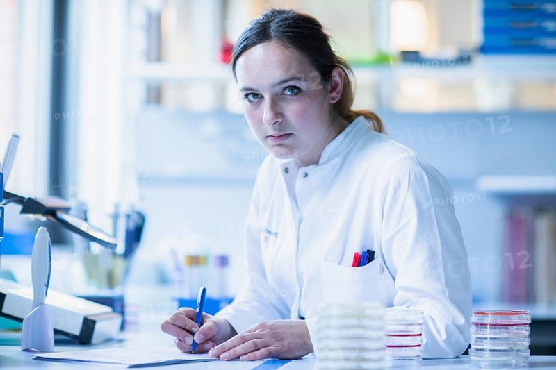 Lab technician with sample in petri dish works in a lab with lab equipment and writes protocol