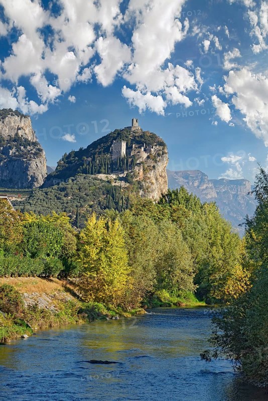 Small idyllic river Sarca with the medieval castle ruin Castello di Arco towering on a castle rock