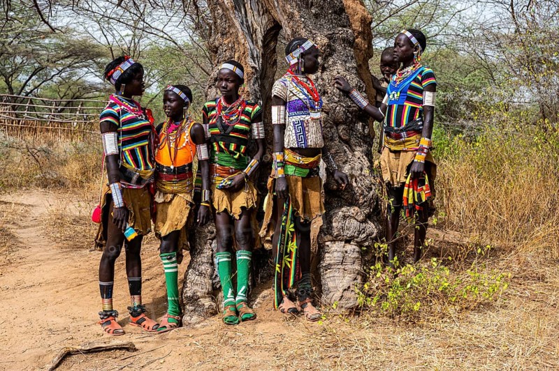 Traditional dressed young girls from the Laarim tribe chatting under a tree