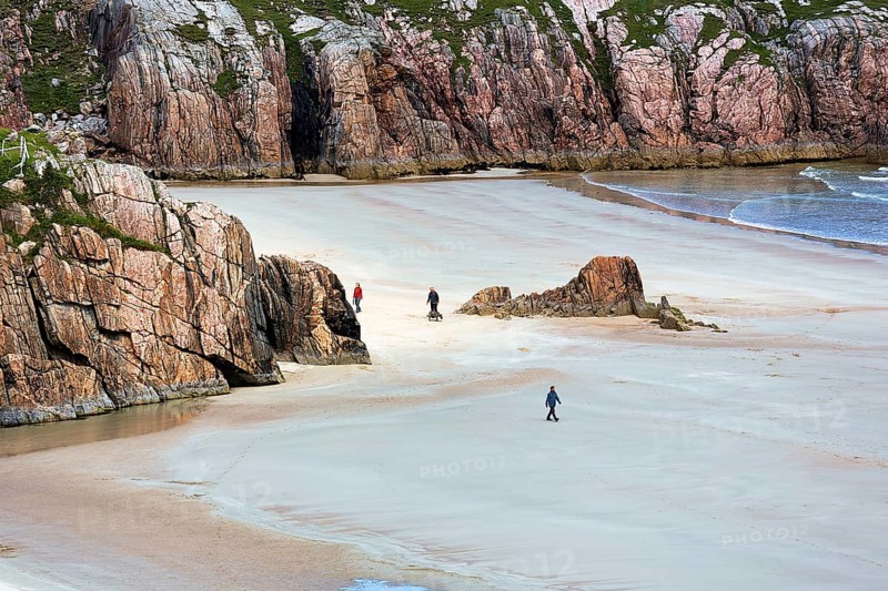 Walkers in bay with rocks and sandy beach