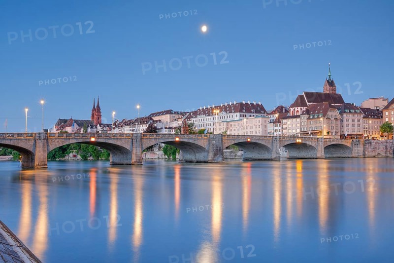 View from the banks of the Rhine along the river promenade to the old town of Basel illuminated at night with the Basel Cathedral