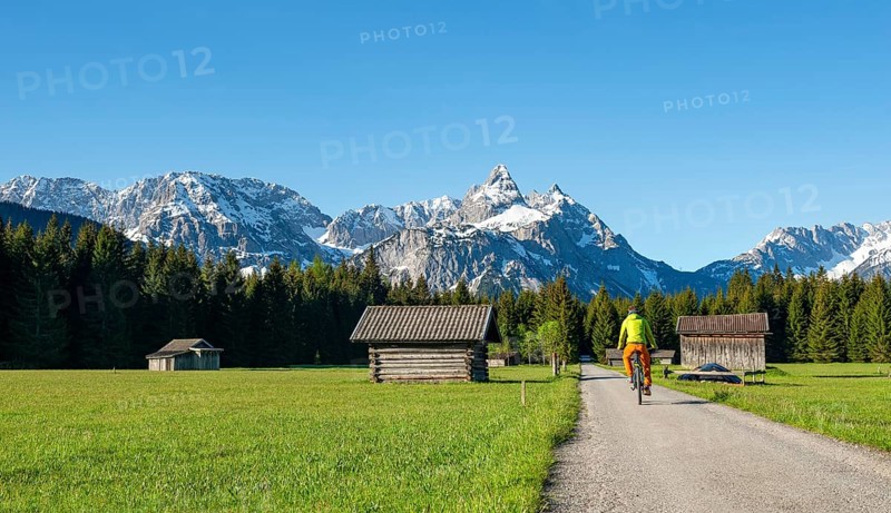 Mountain biker on road through meadow with hay barns