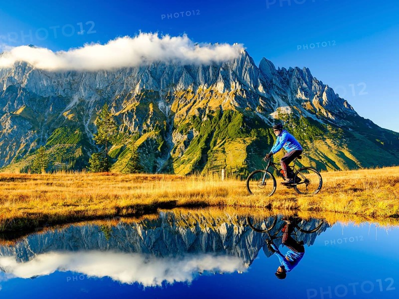Mountain biker in front of mountain scenery reflected in a mountain lake