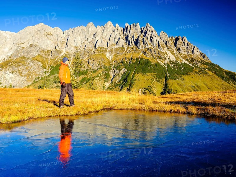Mountaineer in front of mountain scenery reflected in a frozen mountain lake