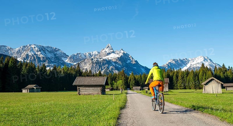 Mountain biker on road through meadow with hay barns