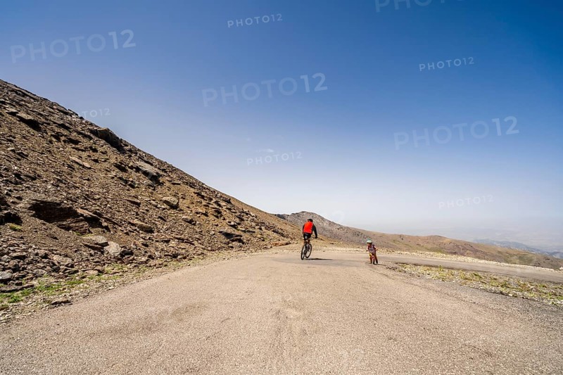Professional cyclist speeding downhill and small boy biker struggling uphill in Sierra Nevada mountains
