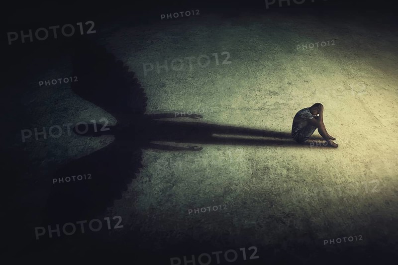 Depressed young man sitting alone isolated in a dark room
