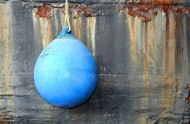 Blue fender in front of rusty ship's wall