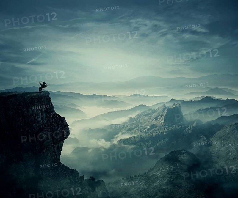 Young man riding a wild horse on the peak of a cliff