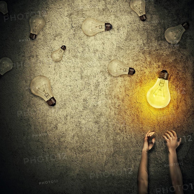 Abstract idea concept as human hands stretched out and juggling with a lot of lightbulbs