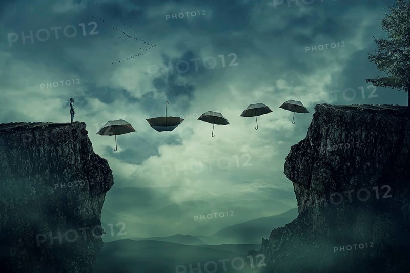 Young boy standing on the peak of a cliff try to pass over valley to another side on a path way of flying umbrellas