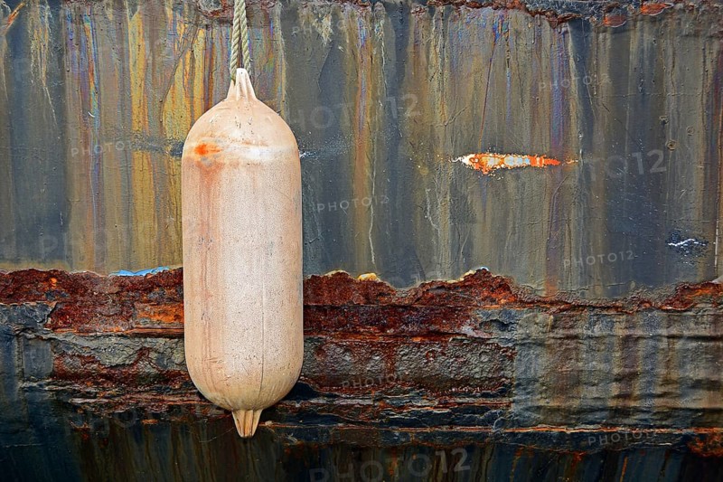 Pink fender in front of rusty ship's wall