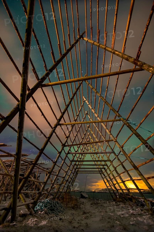 Aurora borealis over a worker in a wooden stockfish rack