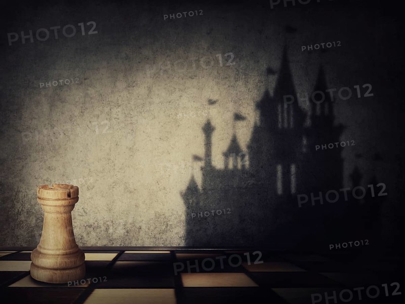 Rook chess piece casting a shadow in shape of a castle on a concrete wall