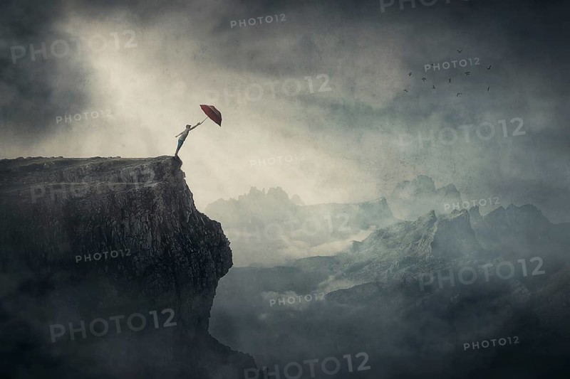 Fearless person on the edge of a cliff determined to catch his umbrella and fly away over abyss