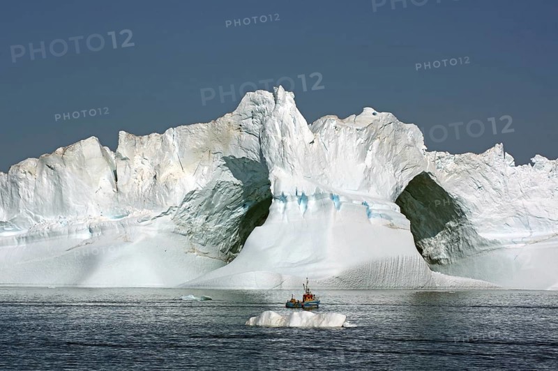 Small fishing boat in front of huge iceberg with two large caves