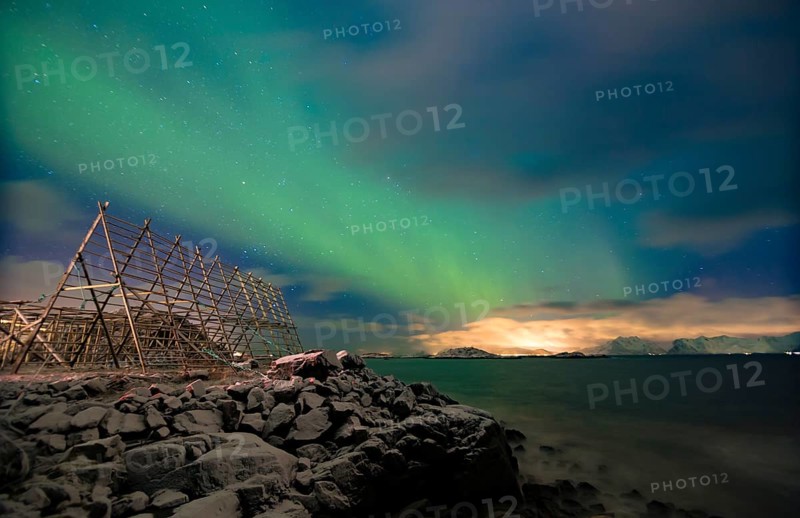 Aurora borealis over a worker in a wooden stockfish rack