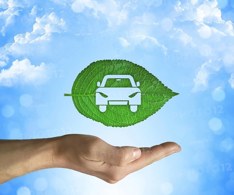 Opened hand holding a green leaf with a car icon inside on a blue sky background