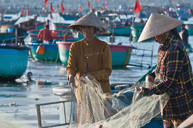 Women in straw hats on the beach checking nets with freshly caught fish and seafood