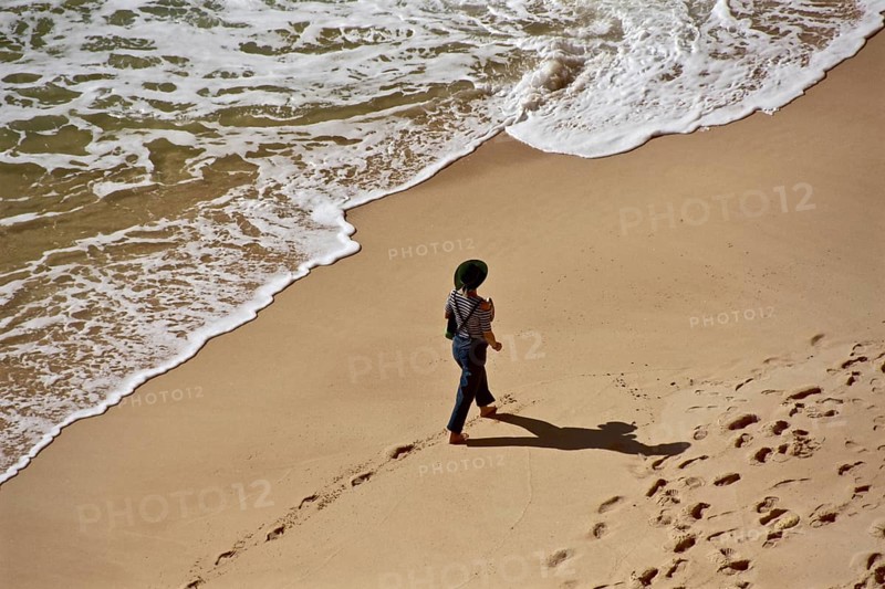 Clothed woman with hat walking on stand in front of wave fringe