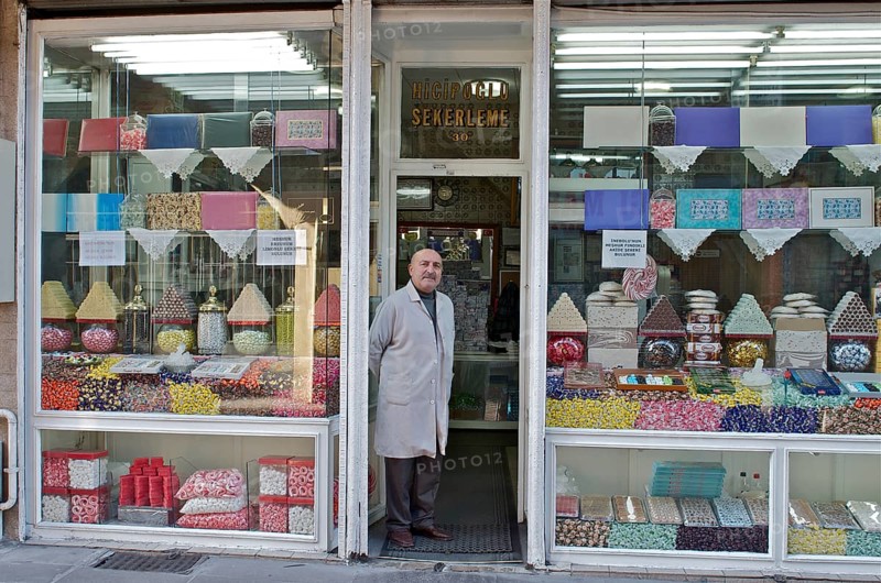 Man in a smock standing in front of his shop with sweets