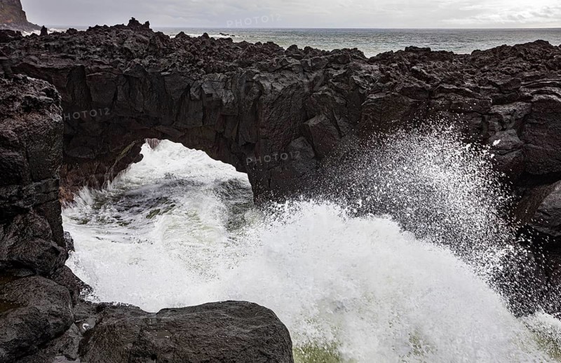 Lava arch on the volcanic coast at high tide with high waves