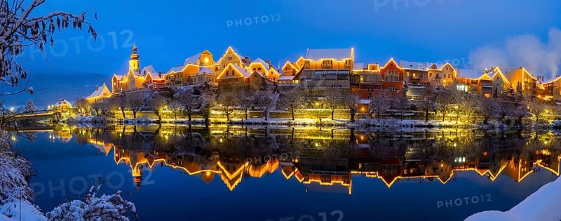 Christmas illuminated house facade of Frohnleiten reflected in the river Mur
