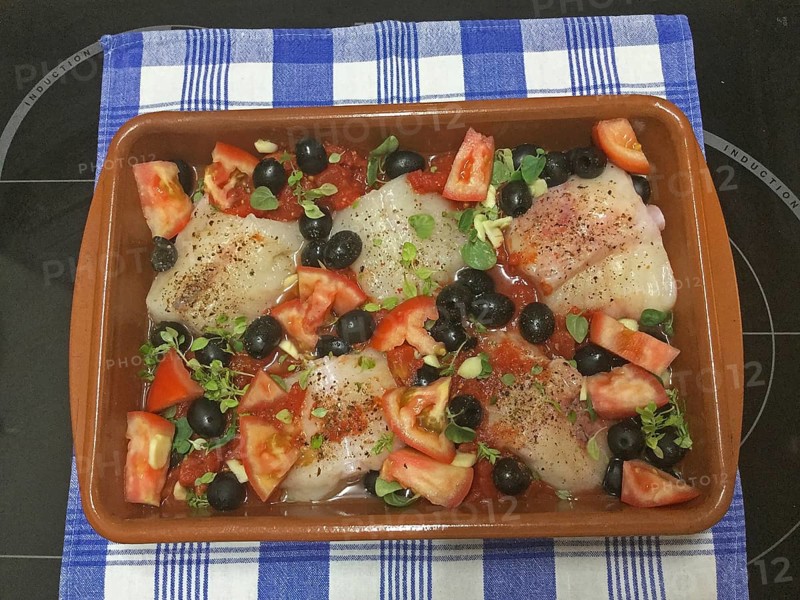 Cod fish in a clay dish with olives