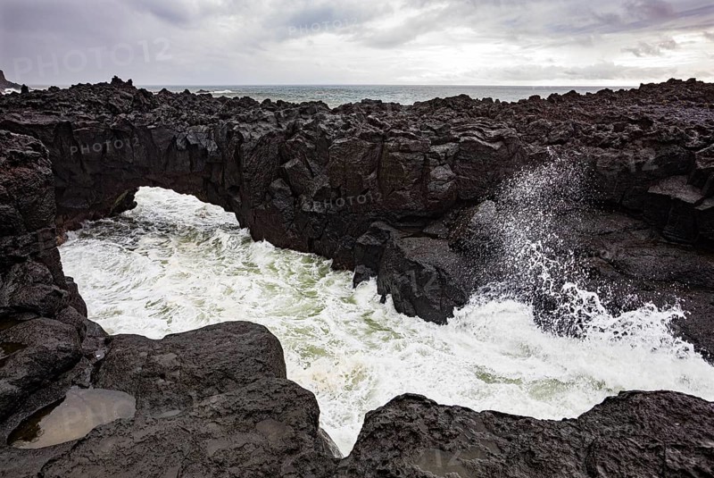 Lava arch on the volcanic coast at high tide with high waves