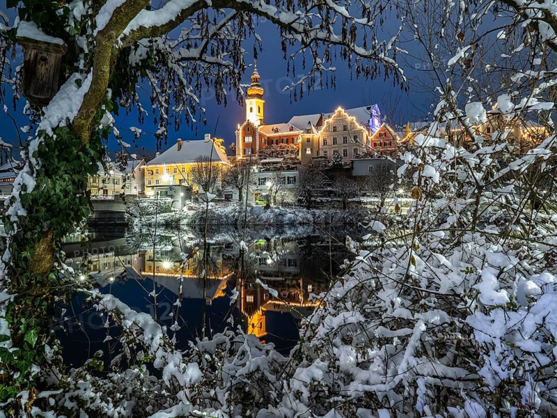 Christmas illuminated house facade of Frohnleiten reflected in the river Mur