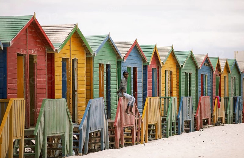 Man sitting on fence in front of colourful beach huts