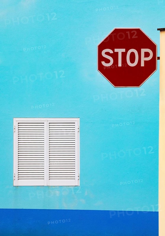 Light blue house facade with closed white shutters and stop sign