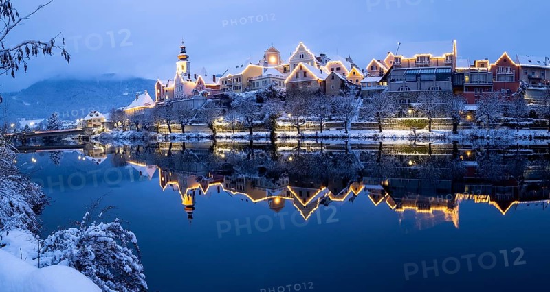 Christmas illuminated house facade of Frohnleiten reflected in the river Mur