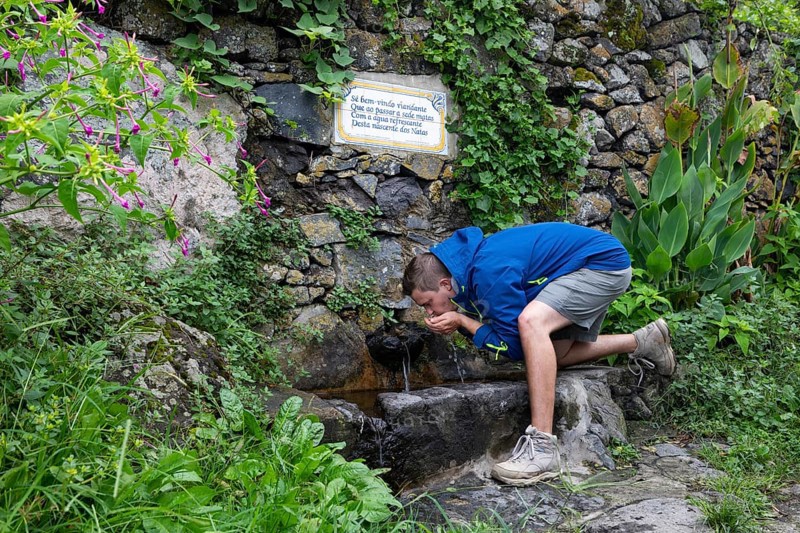 Hiker drinking at the fountain to the path to Rocha da Relva