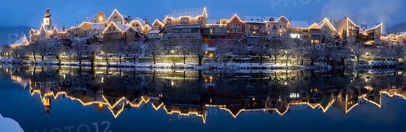 Christmas illuminated house facade of Frohnleiten reflected in the river Mur