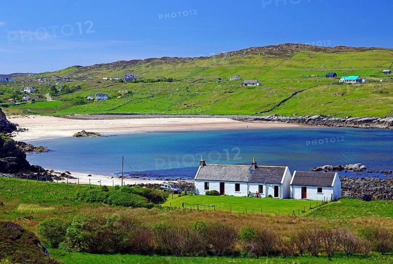 Small cottage in front of long sandy beach in green landscape