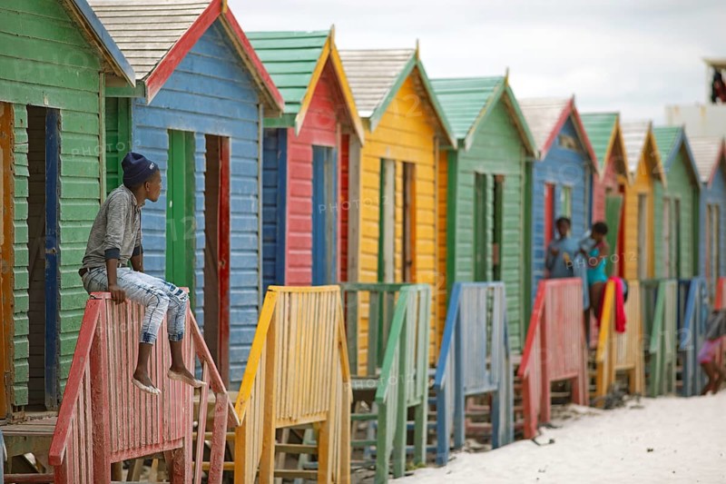 Man sitting on fence in front of colourful beach huts