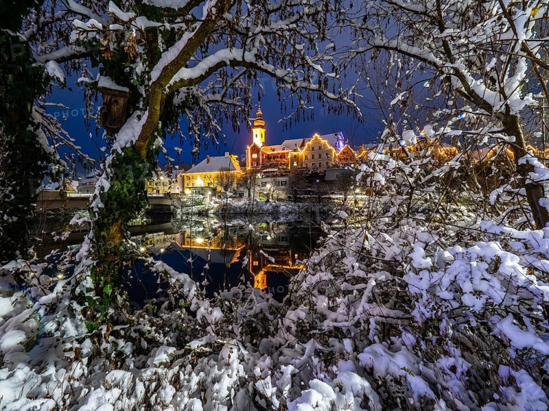 Christmas illuminated house facade of Frohnleiten reflected in the river Mur