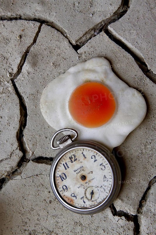 Handless pocket watch with fried egg on dried clay floor