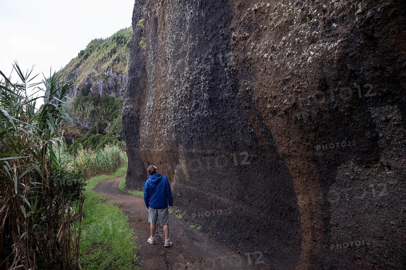 Hikers on the path to Rocha da Relva past eroded lava rocks