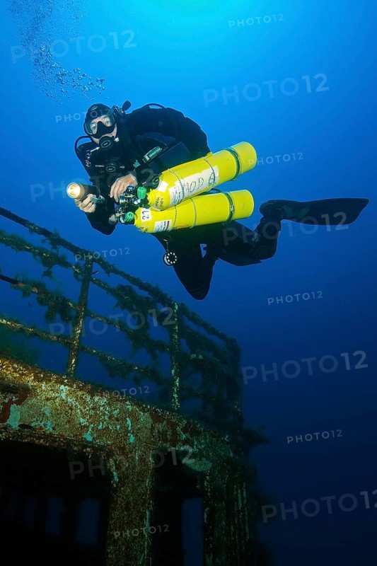 Diver swims over shipwreck has special equipment carries stage tanks for mixed gas diving