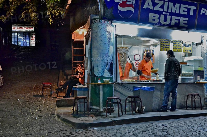 Kebab shop illuminated at night with vendor and customers