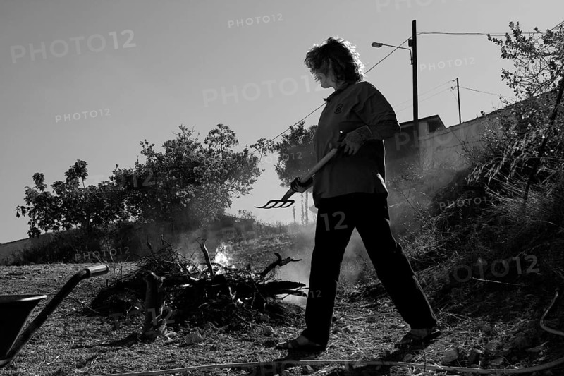Woman with pitchfork in front of fire with garden waste