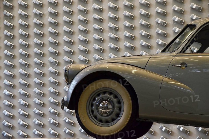 Grey vintage car with whitewall tyres in front of Audi design wall