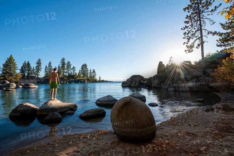 Young man in swimming trunks standing on a round stone in the water