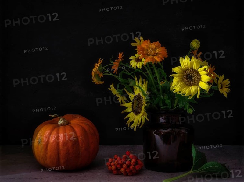 Still life with pumpkin next to rowan berries and autumn flowers in glass