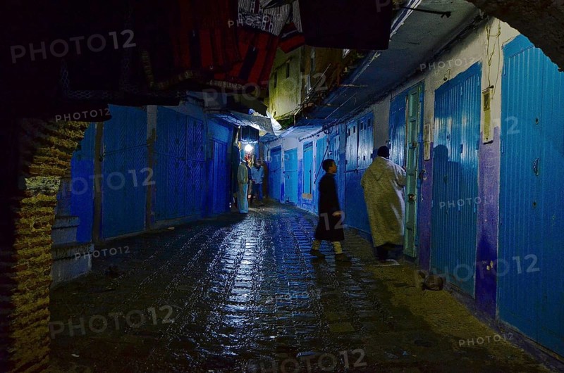 Shopkeepers close door in sparsely lit alley with closed shops at night