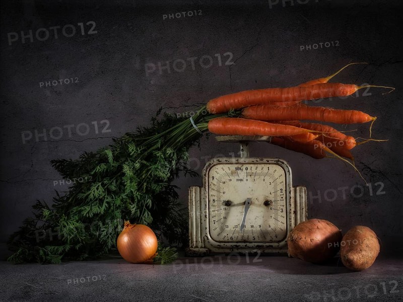 Still life with carrots on old kitchen scales next to onions and sweet potatoes