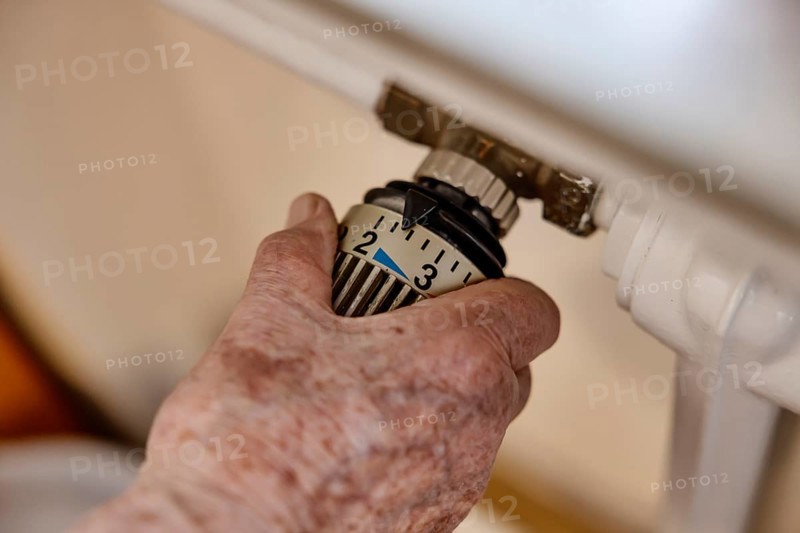 Hand of a senior citizen with age spots on the thermostat of a heater